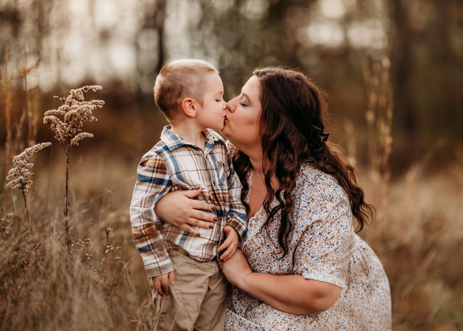 A warm and intimate moment captured between family members sharing a kiss in a rustic outdoor setting during golden hour.
