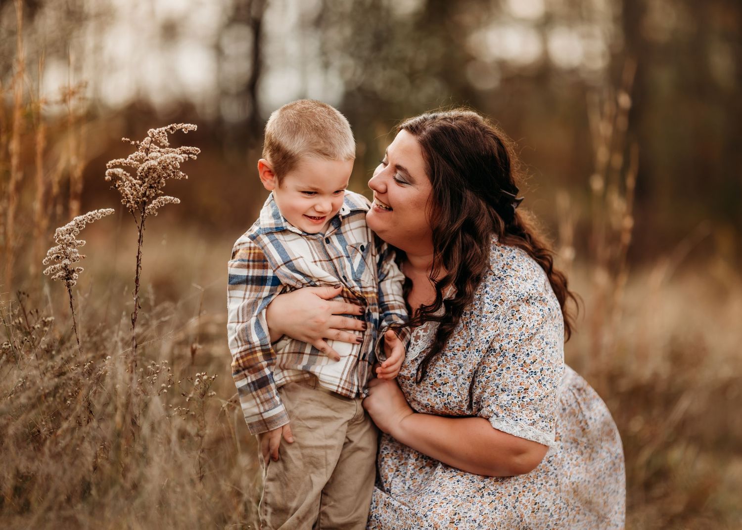 A sweet maternal moment captured in a field of dried grass with warm autumn tones and natural lighting.