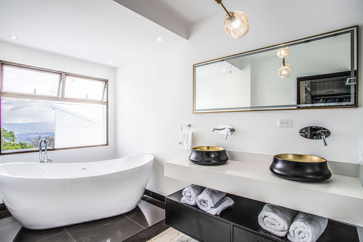Modern bathroom with a freestanding bathtub, double sinks, and a large window offering scenic views
