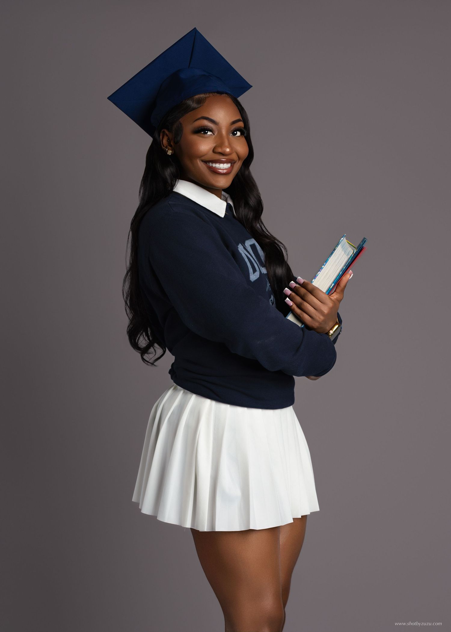 Graduate in lime green dress and academic regalia poses against beige background.