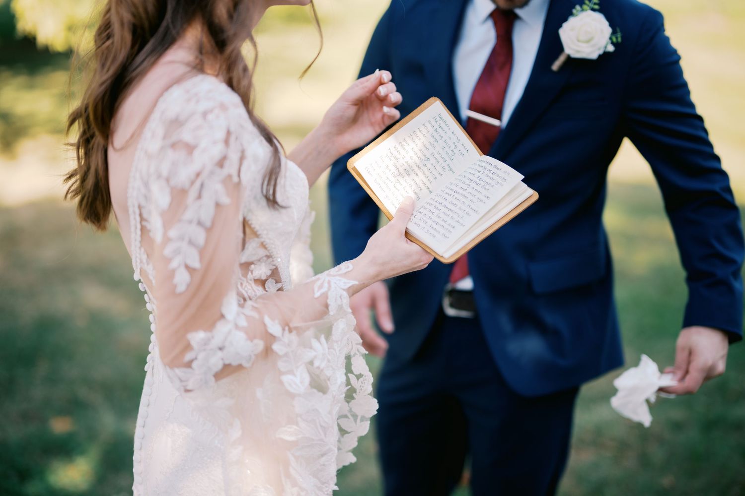 A couple exchanges vows during an outdoor wedding ceremony, with bride in lace dress and groom in navy suit.