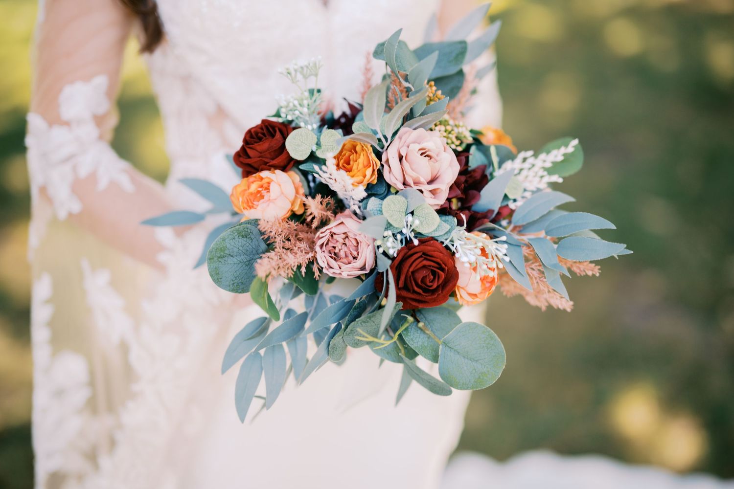 A romantic wedding bouquet features blush pink roses, burgundy blooms, and soft eucalyptus leaves in natural light.