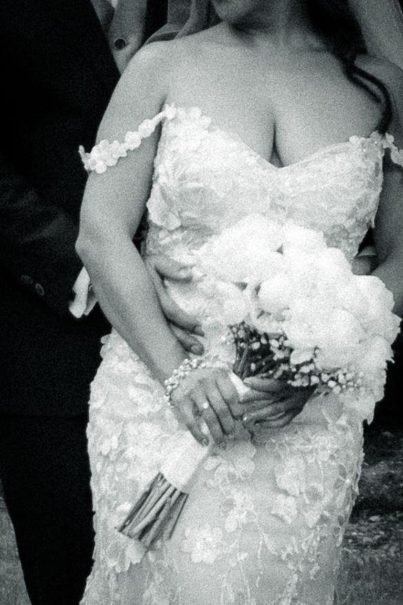 Close-up of detailed lace wedding dress and bouquet in black and white.