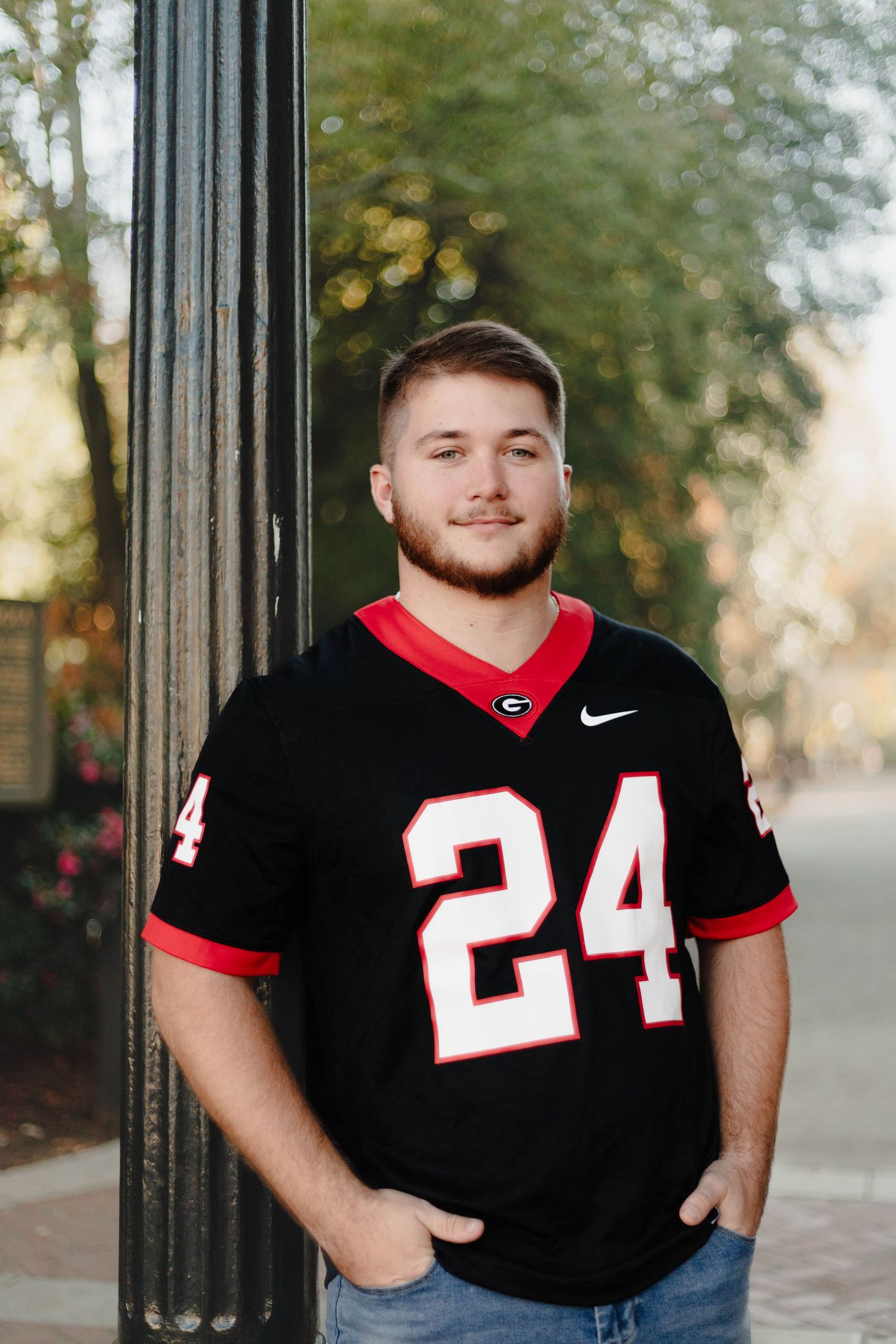 Sports fan wearing Georgia Bulldogs jersey poses against black column.