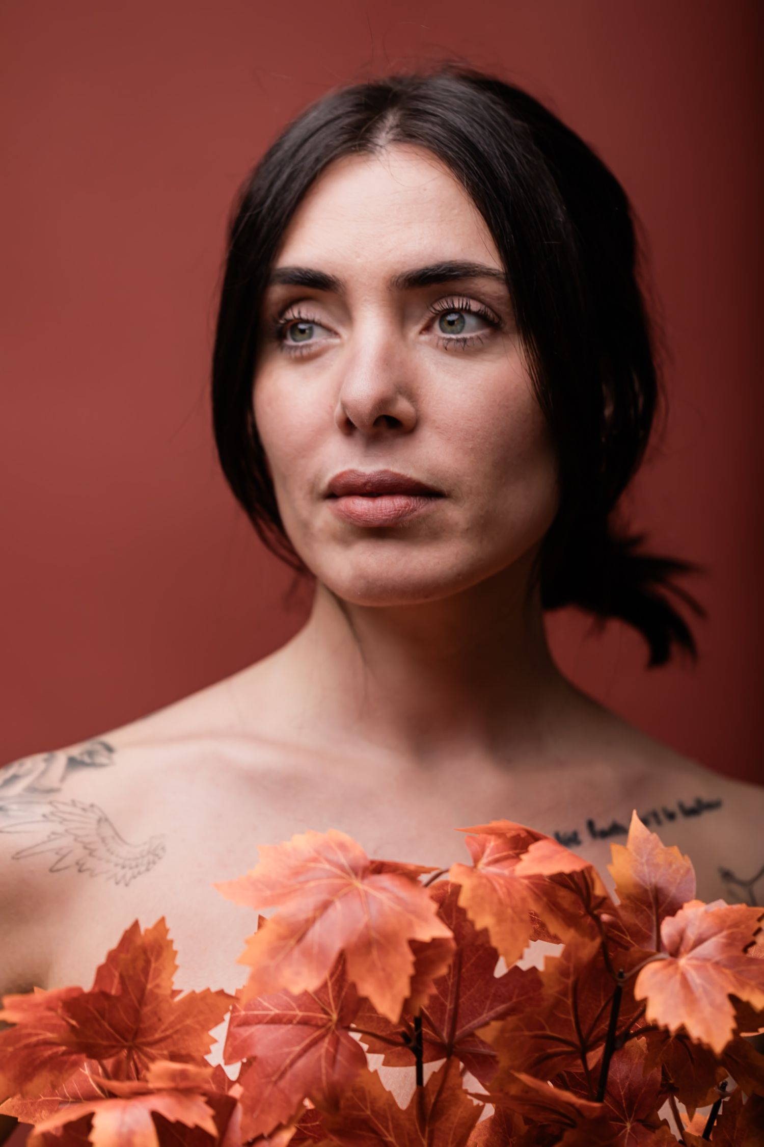 Artistic portrait with autumn leaves featuring soft lighting against terracotta background.