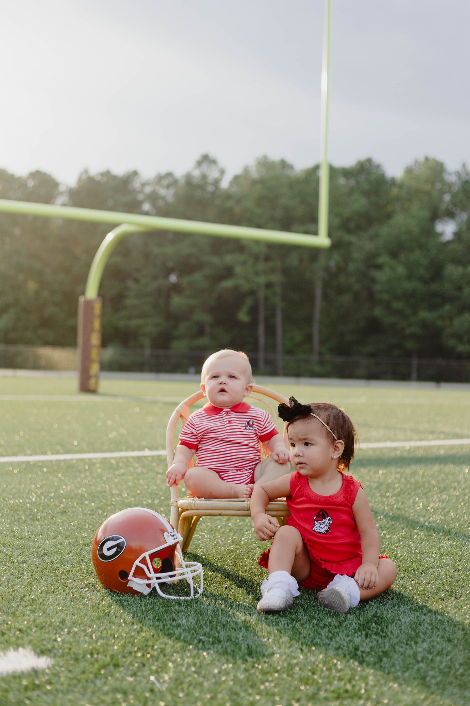 Two young children sitting on football field with Georgia Bulldogs helmet.