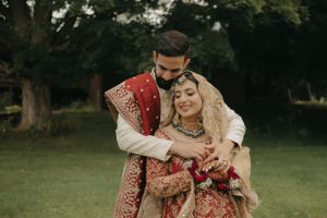 Romantic embrace between couple wearing traditional South Asian wedding attire in garden setting.