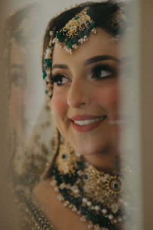 Artistic portrait showcasing elaborate South Asian bridal makeup, jewelry and embroidered dress details.