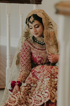 Traditional South Asian bridal attire in deep red with intricate gold embroidery.
