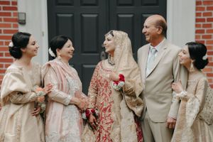 A wedding party in traditional South Asian attire poses together on brick building steps.