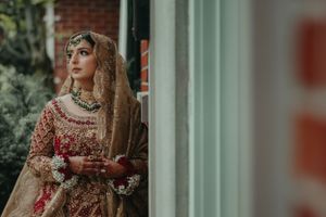 Elegant bridal portrait featuring traditional South Asian wedding attire by a window.
