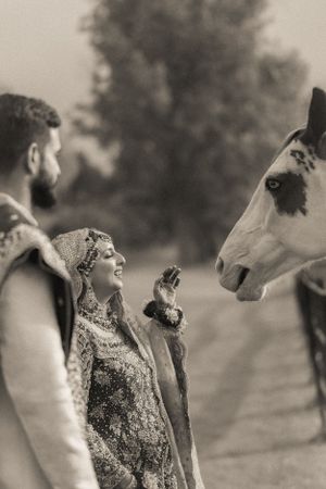 Black and white portrait of couple interacting with horse during their wedding photoshoot.