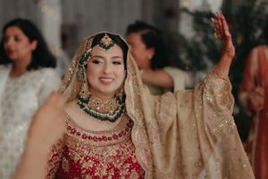 Bride in traditional red and gold South Asian wedding attire with ornate jewelry.