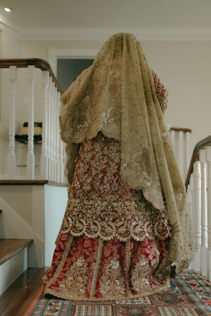 Traditional bridal lehenga with intricate embroidery and golden veil displayed on staircase.