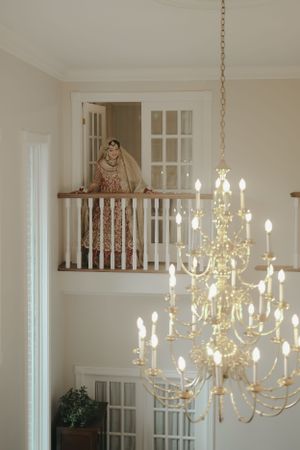 Elegant chandelier and bride in traditional attire photographed from lower level of grand staircase.