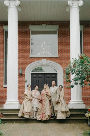 A wedding party poses on the steps of a classic brick building with white columns.