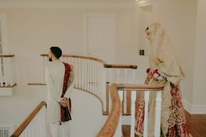 A couple in traditional wedding attire stands on opposite sides of an elegant staircase.
