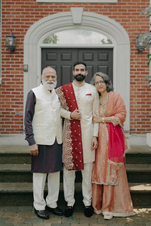 Three people in traditional South Asian formal wear pose together on building steps.
