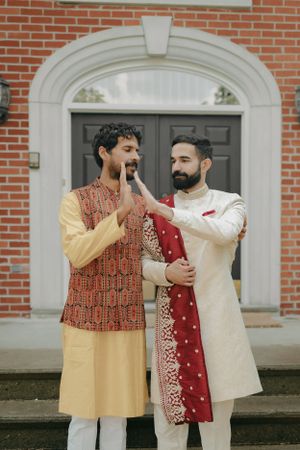 Two people in traditional South Asian formal wear share a lighthearted moment outside a brick building.