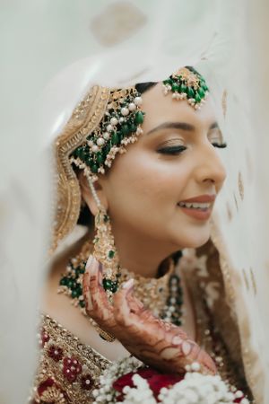 Close-up of bridal details showing emerald and gold jewelry with intricate henna-adorned hands.