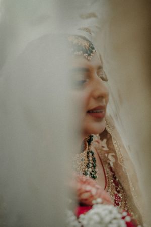 Traditional South Asian bride wearing intricate jewelry and veil captured in dreamy soft focus portrait.