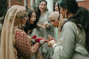 A group gathers around to admire jewelry details during a South Asian wedding celebration.