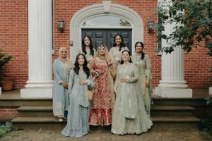 A group in coordinated formal South Asian attire poses on brick building steps for a wedding photo.