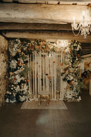 Wedding ceremony backdrop featuring white string curtains and floral arrangements in a rustic stone venue.
