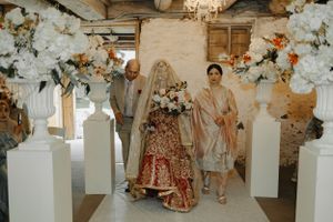 Wedding party poses in an elegantly decorated rustic venue with white pedestals and floral arrangements.
