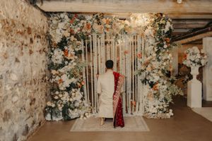 Wedding ceremony setup with floral arch and string curtain backdrop in a rustic stone-walled venue.