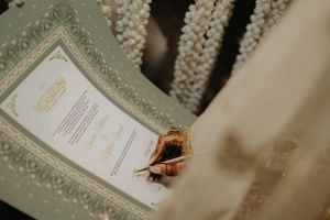 Close-up of a hand signing an ornate wedding invitation or certificate.