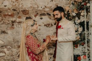 A couple in traditional South Asian wedding attire sharing an intimate moment against a rustic backdrop.