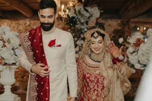 Newlyweds in traditional South Asian wedding attire pose in an elegant rustic venue.