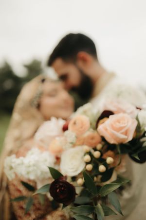 Romantic wedding portrait with soft focus on peach and cream rose bouquet in foreground.
