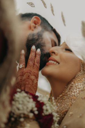 Traditional Indian wedding couple shares an intimate moment showcasing intricate henna designs and elegant attire.