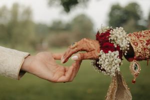 Two hands reach toward each other during a traditional wedding ceremony with intricate henna designs.