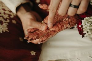 Close-up of hands with intricate henna designs against traditional red and white wedding attire.