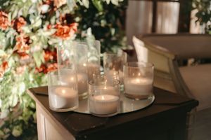Collection of glass candle holders with lit candles against a floral backdrop.
