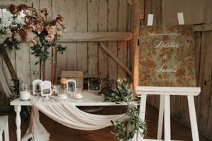 Rustic wedding decor setup with draped fabric and floral arrangements against a wooden wall.