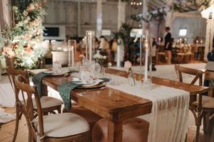 Elegantly set wedding reception table with wooden chairs and white table runner.