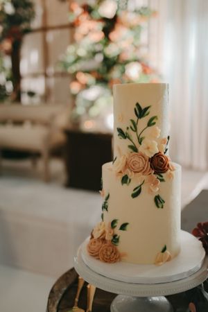 Elegant white wedding cake decorated with sugar flowers and green foliage on a cake stand.