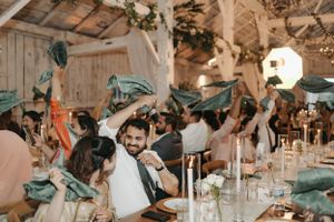 Wedding reception celebration in a rustic barn with guests waving teal napkins.