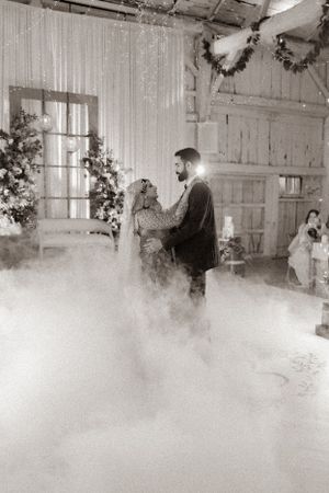 Couple shares romantic moment on foggy dance floor with string lights and floral decor.