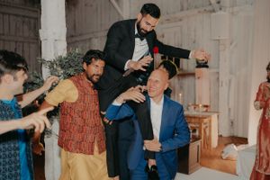 A lively pre-wedding celebration with guests pouring drinks and socializing in a rustic indoor setting.