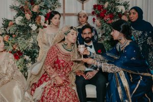 Wedding celebration gathering with guests in traditional South Asian attire around floral backdrop.