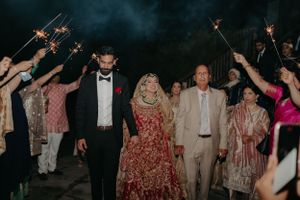 Wedding guests hold sparklers creating a magical exit tunnel for the newlyweds in traditional attire.