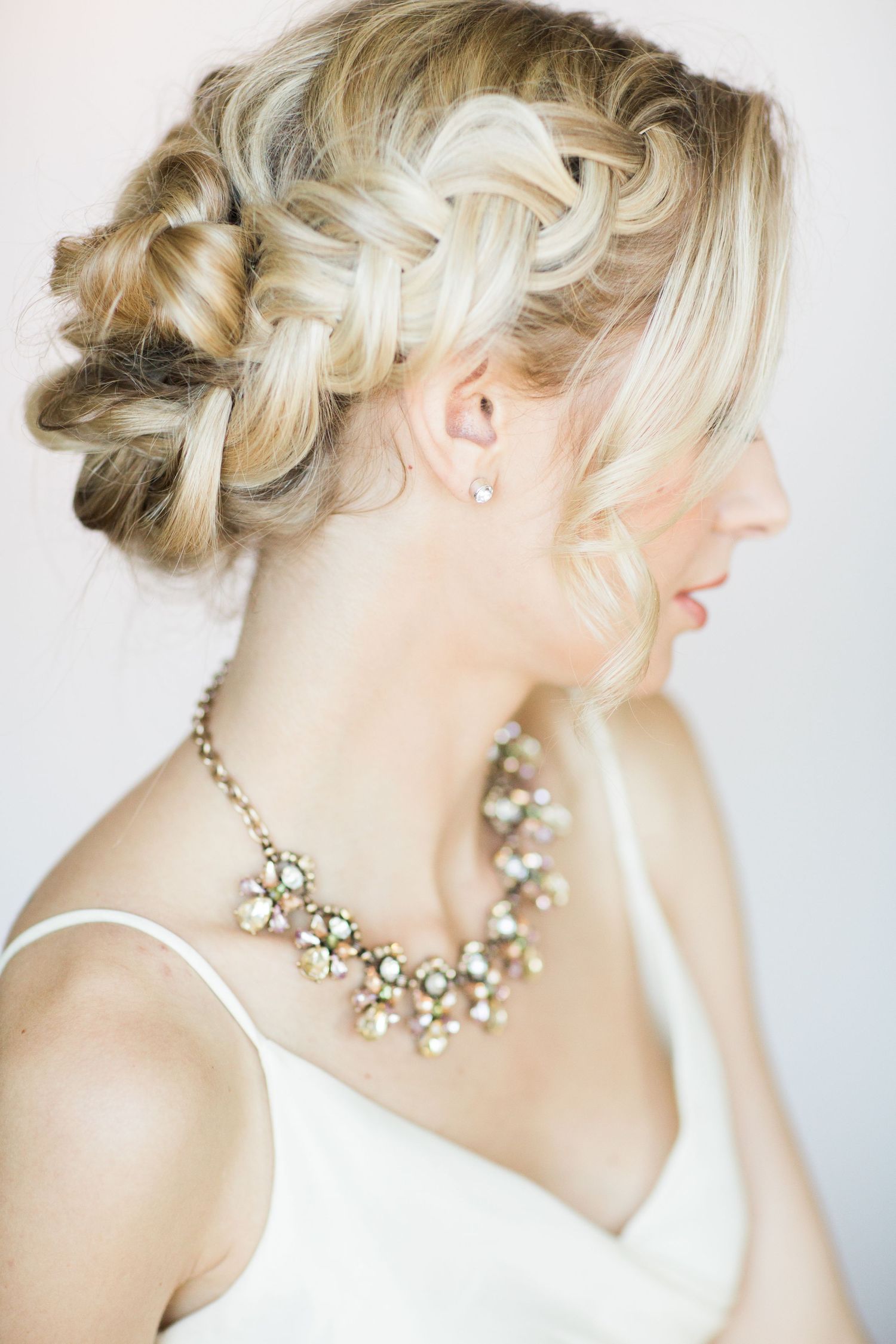 Elegant bridal hairstyle with intricate braided updo and statement crystal necklace against light background.