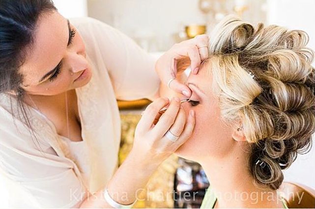 Makeup artist applies finishing touches to bridal beauty preparation in a warm, softly lit setting.