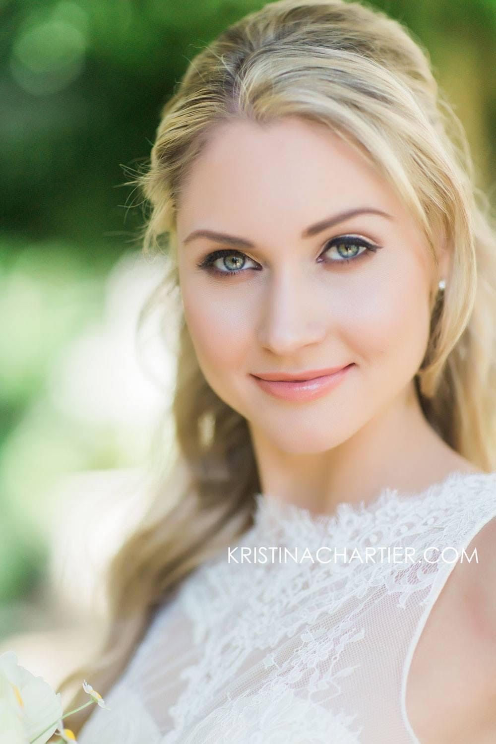 Elegant bridal portrait with soft lighting and lace dress details against a blurred green natural background.