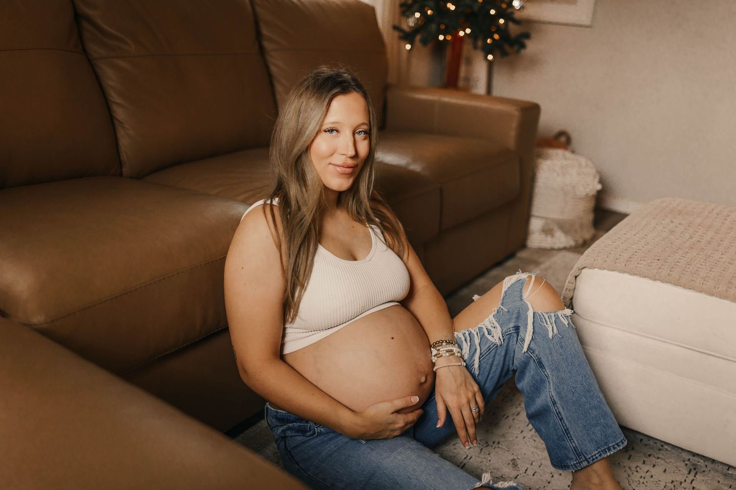 An expectant mother in jeans relaxes on a brown leather couch.